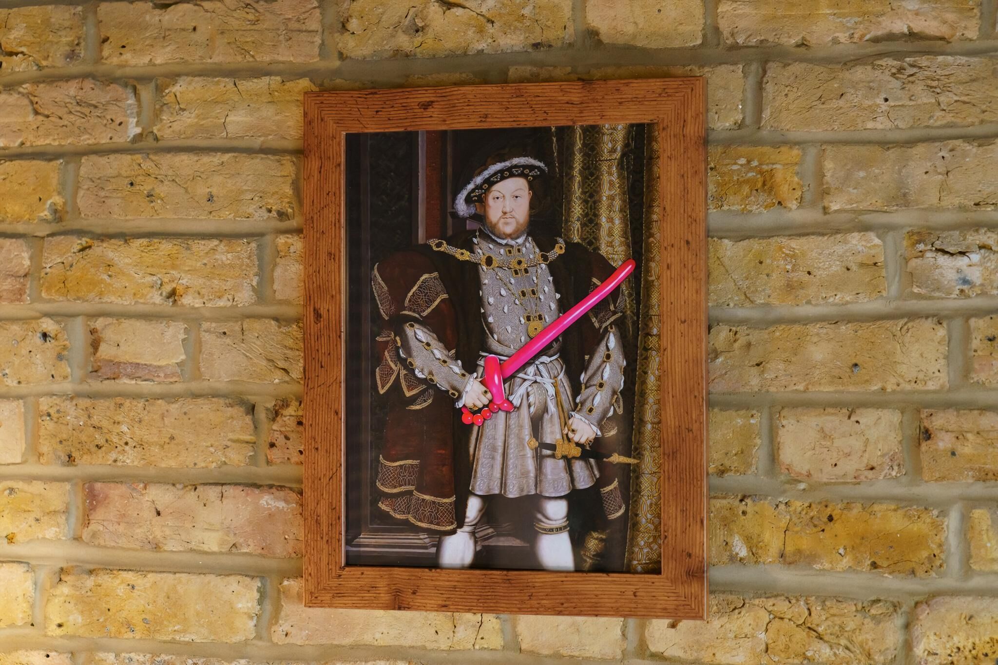 A framed portrait of a historical figure in period attire, mounted on a brick wall.