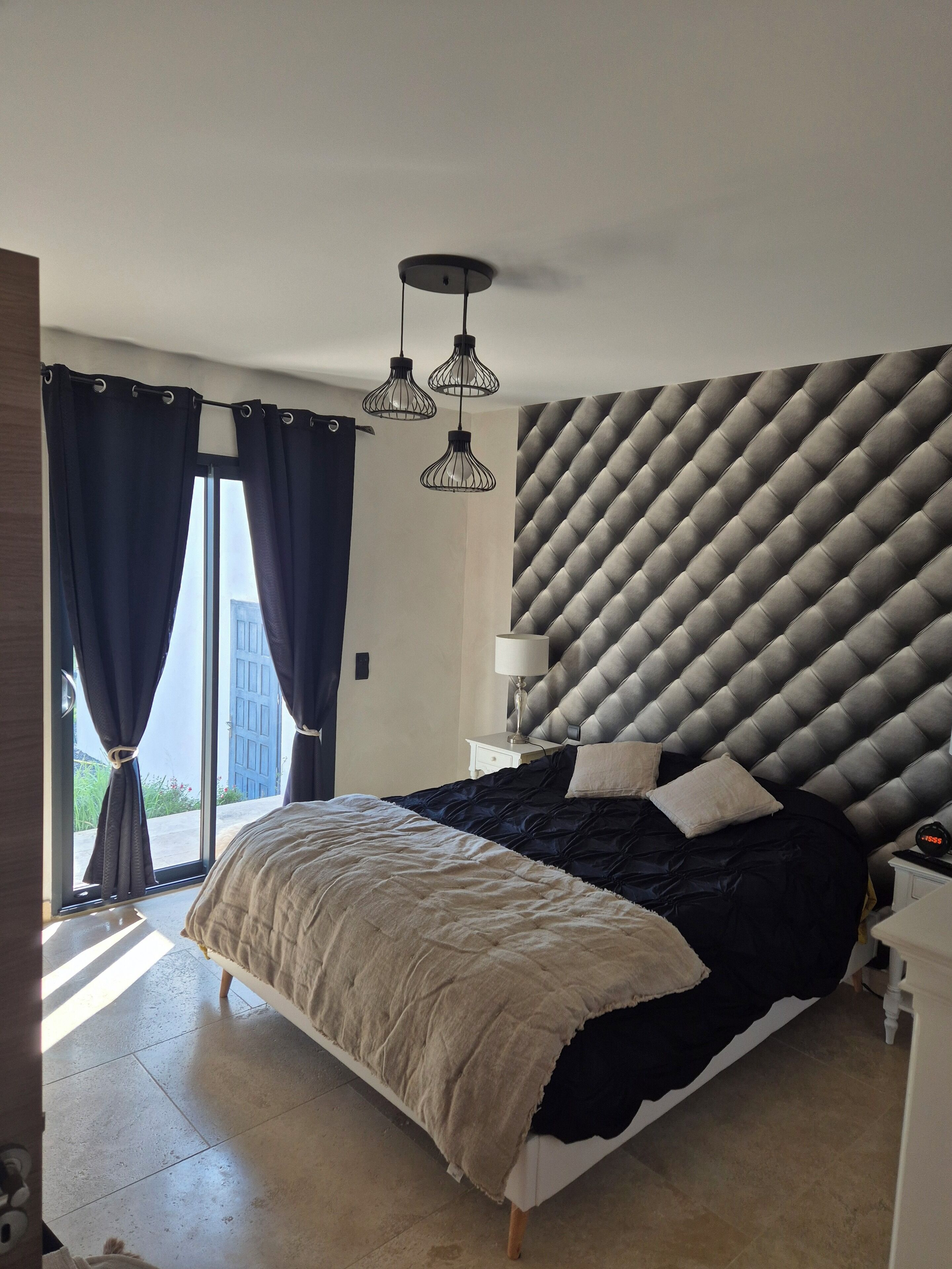 A bedroom with a bed, a nightstand, a lamp, and a wall with a geometric pattern.