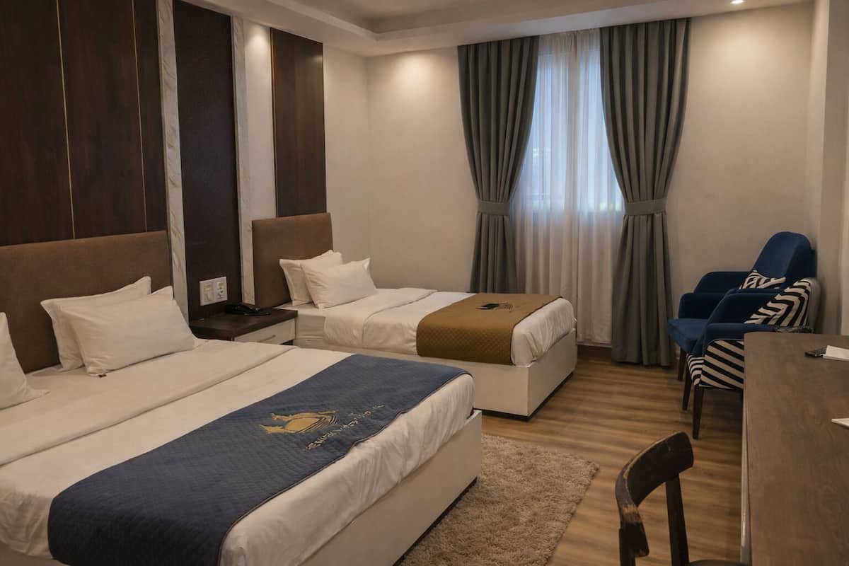 Une chambre d’hôtel avec deux lits, un bureau, une chaise et une fenêtre avec des rideaux.