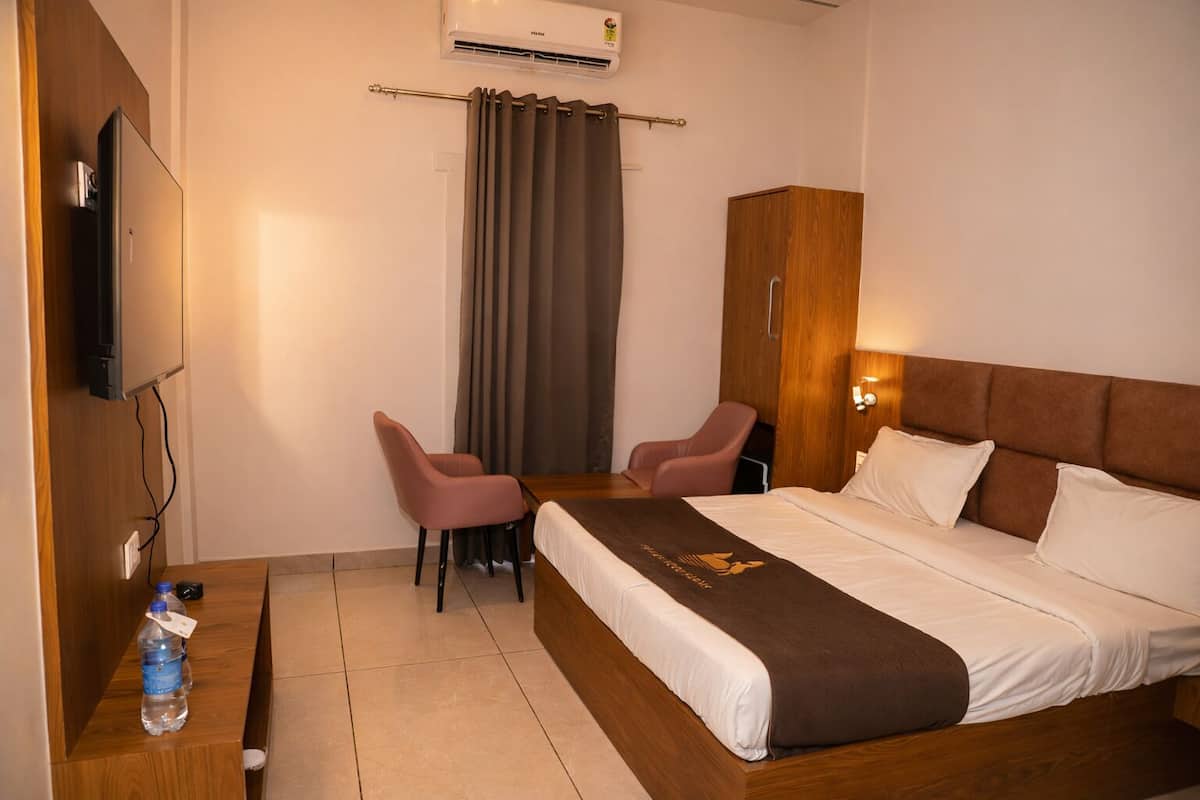 Une chambre d’hôtel comprenant un lit, deux chaises, une armoire en bois, un téléviseur et un appareil de climatisation.