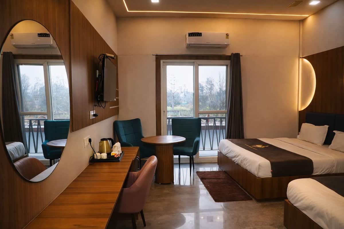 Une chambre d’hôtel comprenant un lit, un bureau, une chaise, une table ronde et un grand miroir. Il y a deux fenêtres avec des rideaux, et un appareil de climatisation est fixé au mur.