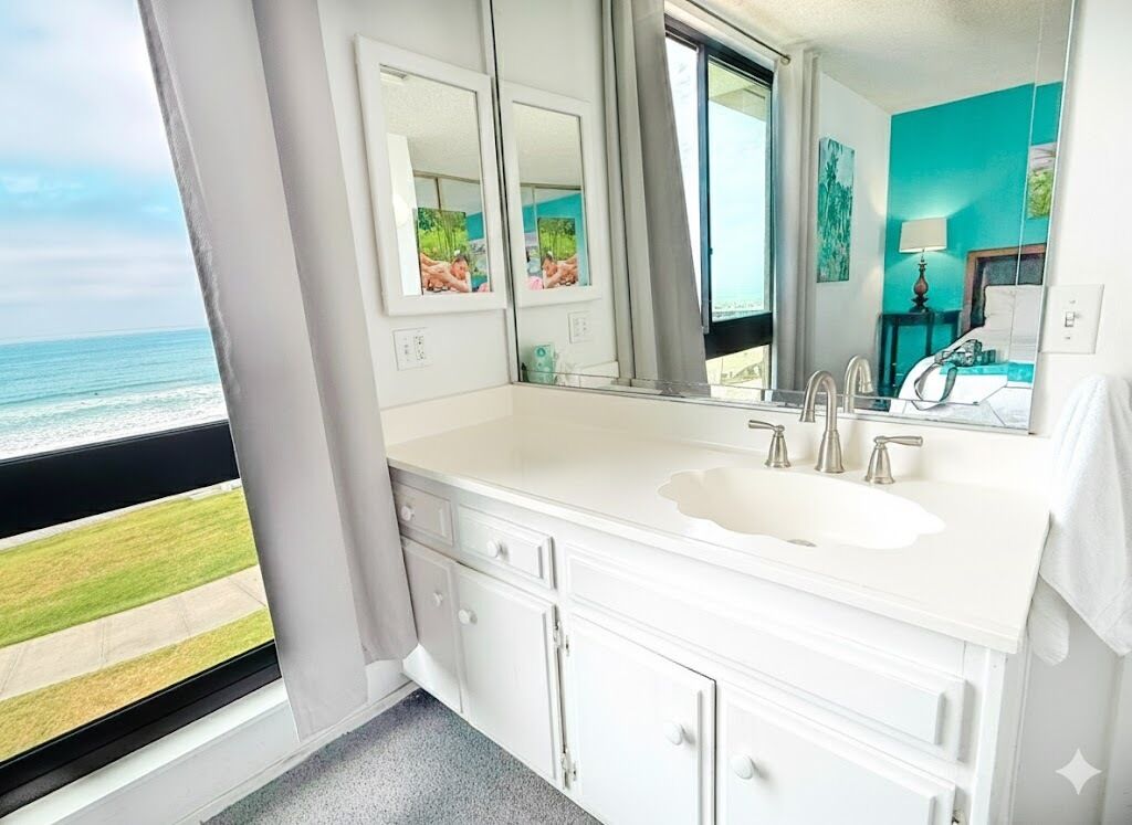 A bathroom with a white vanity, a large mirror, and a view of the ocean.