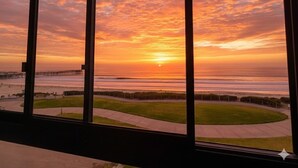 A sunset view from a window overlooking a beach with a pier and a grassy area. - Ocean Views * Corner Unit * POOL & HOT TUB (San Diego)