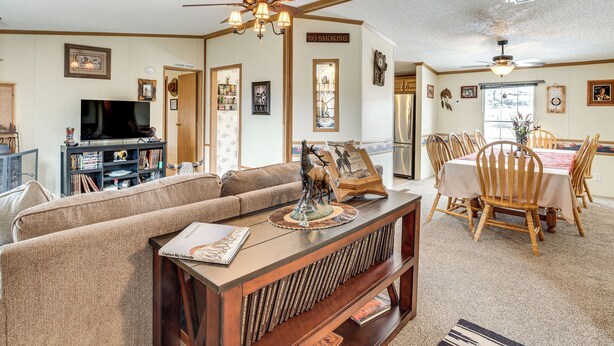 A cozy living room with a sofa, a coffee table with books, a dining area with a table and chairs, and a ceiling fan. - Hike, Fish & Unwind: Mtn-view Gem in Cedaredge! (Cedaredge)