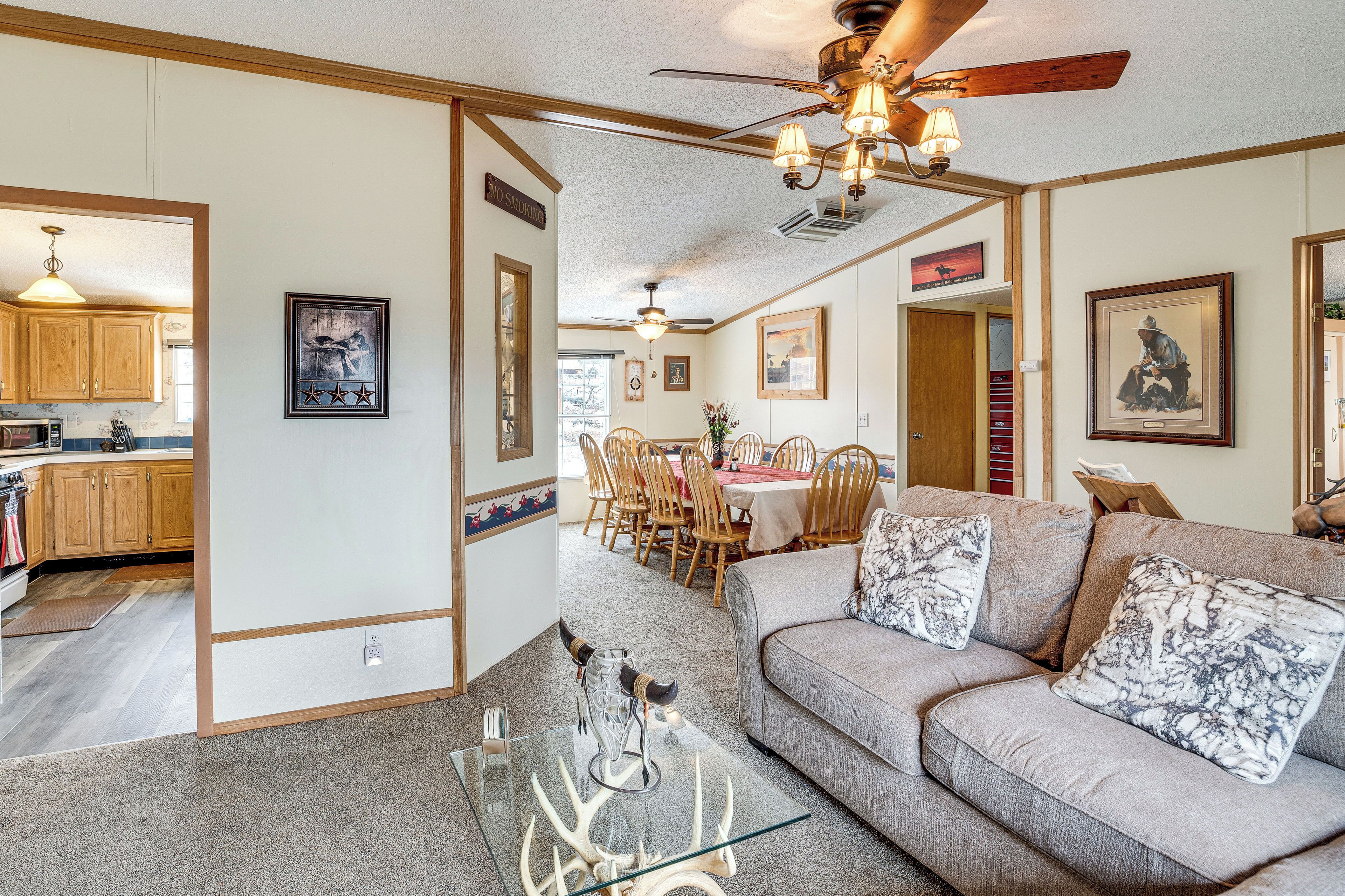 A spacious living area with a glass coffee table, a sofa with patterned cushions, and a ceiling fan.