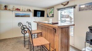 A small, cozy room with a wooden bar counter, two metal chairs, a television mounted on the wall, and a window providing a view of the outside. - Hike, Fish & Unwind: Mtn-view Gem in Cedaredge! (Cedaredge)