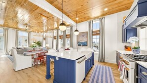 A modern kitchen with a central island, wooden ceiling, and large windows. - Designer Coastal Cottage with Lake Views and 3 King Suites at Cinnamon Shore (Port Aransas)