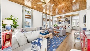A modern living room with a wooden ceiling, large windows, and a dining area. - Designer Coastal Cottage with Lake Views and 3 King Suites at Cinnamon Shore (Port Aransas)