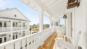 A white building with a covered balcony, wooden flooring, and a view of the surrounding area. - Designer Coastal Cottage with Lake Views and 3 King Suites at Cinnamon Shore (Port Aransas)