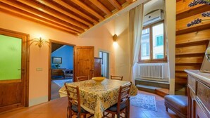 Un'area pranzo con soffitto in legno, un tavolo con sedie e vista su una stanza con finestra e termosifone.