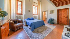 Una camera da letto con un letto, una poltrona, un armadietto in legno, un termosifone e una finestra.