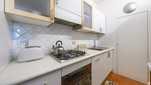 Una cucina compatta con pensili bianchi, un fornello a gas, un tostapane e una sveglia appesa al muro.