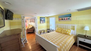 A bedroom with a bed, bedside tables, a dresser, a television, and a window with blinds. - Coquina Cottage - close to town - wifi - Linens and Towels are provided (Chincoteague)