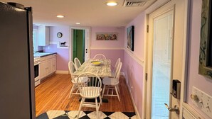 A compact kitchen with wooden cabinets, a dining table with chairs, and a patterned rug. - Coquina Cottage - close to town - wifi - Linens and Towels are provided (Chincoteague)