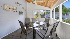 A covered patio with a glass table and chairs, a ceiling fan, and decorative fish on the wall. - Coquina Cottage - close to town - wifi - Linens and Towels are provided (Chincoteague)
