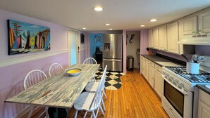 A kitchen with wooden flooring, white cabinets, a stainless steel refrigerator, and a stove. - Coquina Cottage - close to town - wifi - Linens and Towels are provided (Chincoteague)