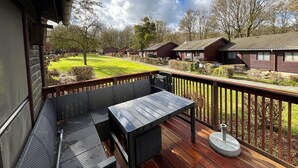 Eine Holzdar Terrasse mit Tisch und Stühlen, mit Blick auf eine Rasenfläche und mehrere Blockhütten.