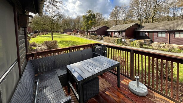 Eine Holzdar Terrasse mit Tisch und Stühlen, mit Blick auf eine Rasenfläche und mehrere Blockhütten.