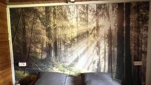 Ein Schlafzimmer mit einer großen Waldmalerei an der Wand, einem Bett mit grauer Bettwäsche und zwei Nachttischen mit Lampen.