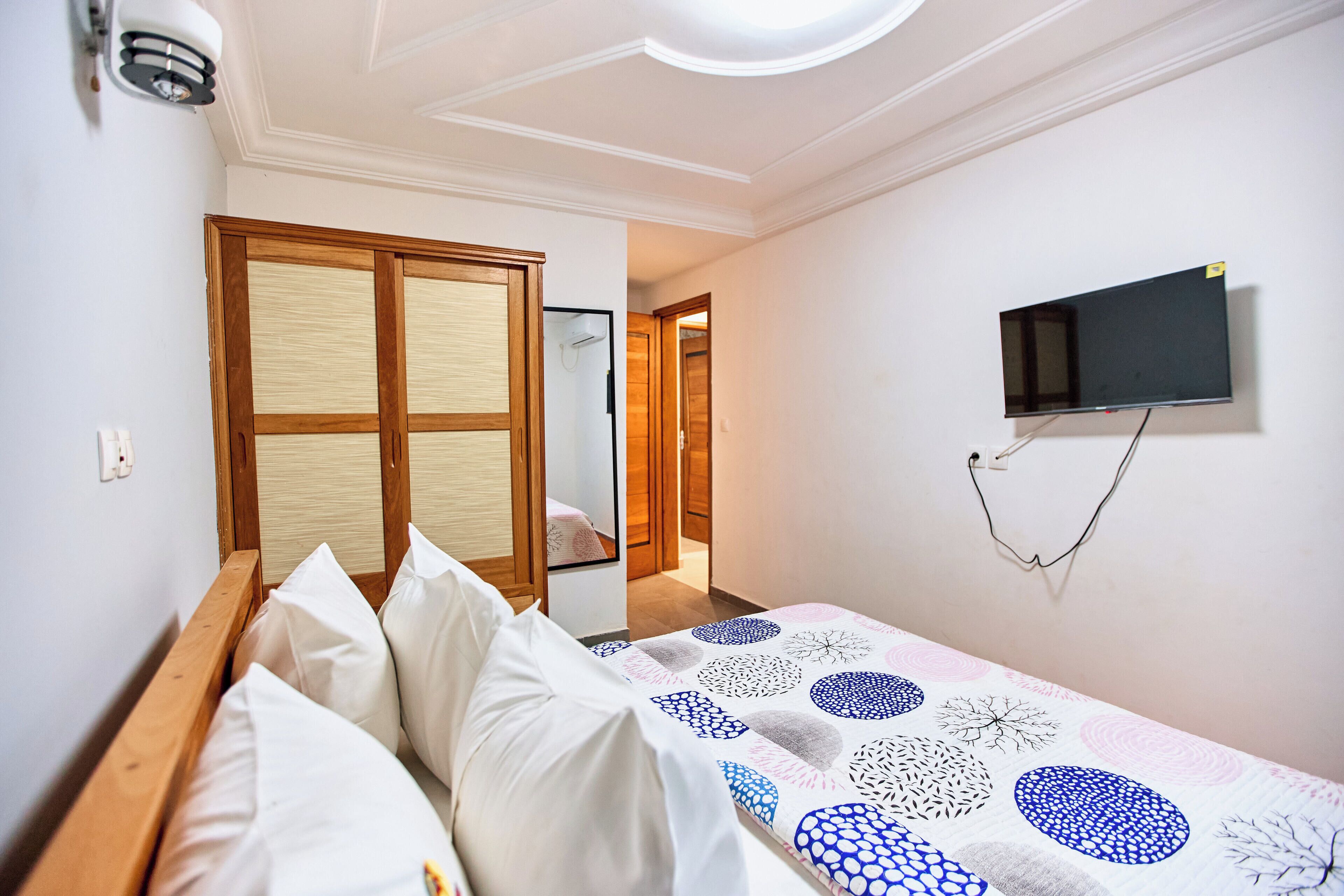 A bedroom with a bed, a TV mounted on the wall, and a wooden wardrobe.