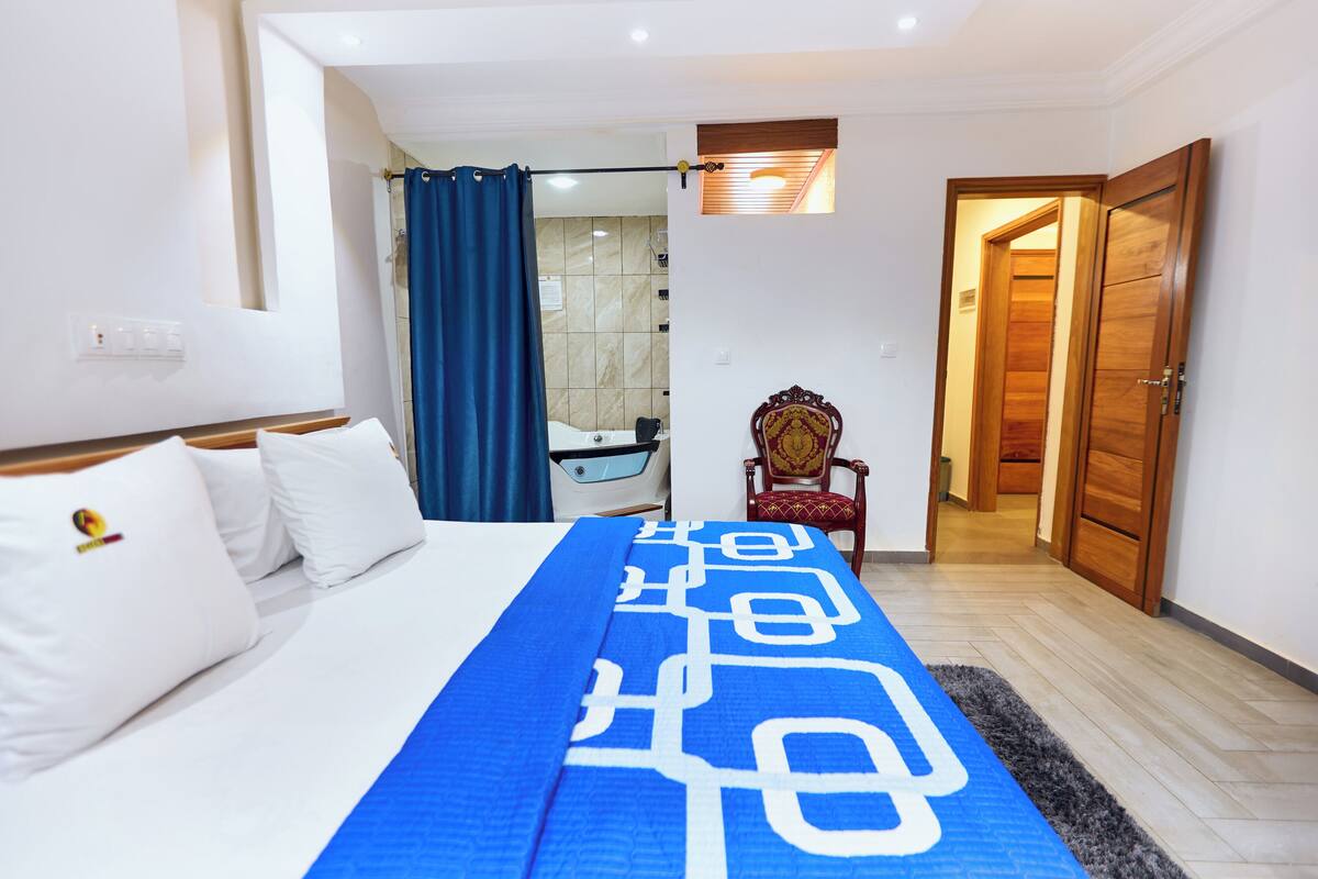 A hotel room with a bed, a shower, a wooden wardrobe, and a chair.