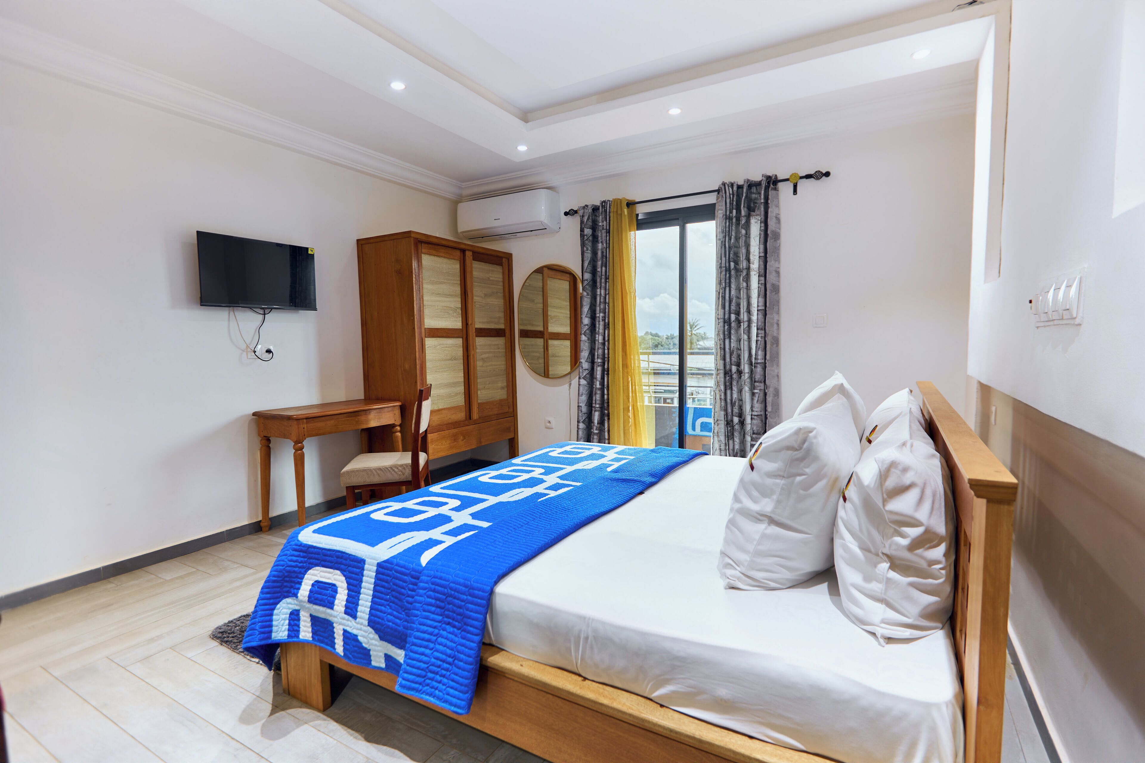 Un dormitorio con cama, escritorio, televisión y ventana con cortinas.