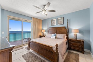 A bedroom with a large bed, a ceiling fan, a nightstand with a lamp, and a view of the ocean through a sliding door. - NEW Treasure Island 911-Heated Pool, Hot Tub, Grills, FREE Beach Service&Golf (Panama City Beach)