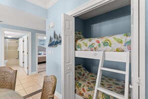 A room with bunk beds, a door, a chair, and a wall with a sailboat painting. - NEW Treasure Island 911-Heated Pool, Hot Tub, Grills, FREE Beach Service&Golf (Panama City Beach)