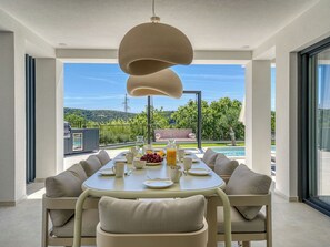 A dining area with a table set for four, outdoor seating, a pool, and a view of the landscape.