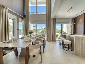 A modern dining area with a long table, chairs, and a bar with stools.