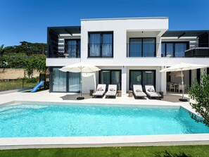 A modern two-story house with a swimming pool, outdoor seating, and a slide.
