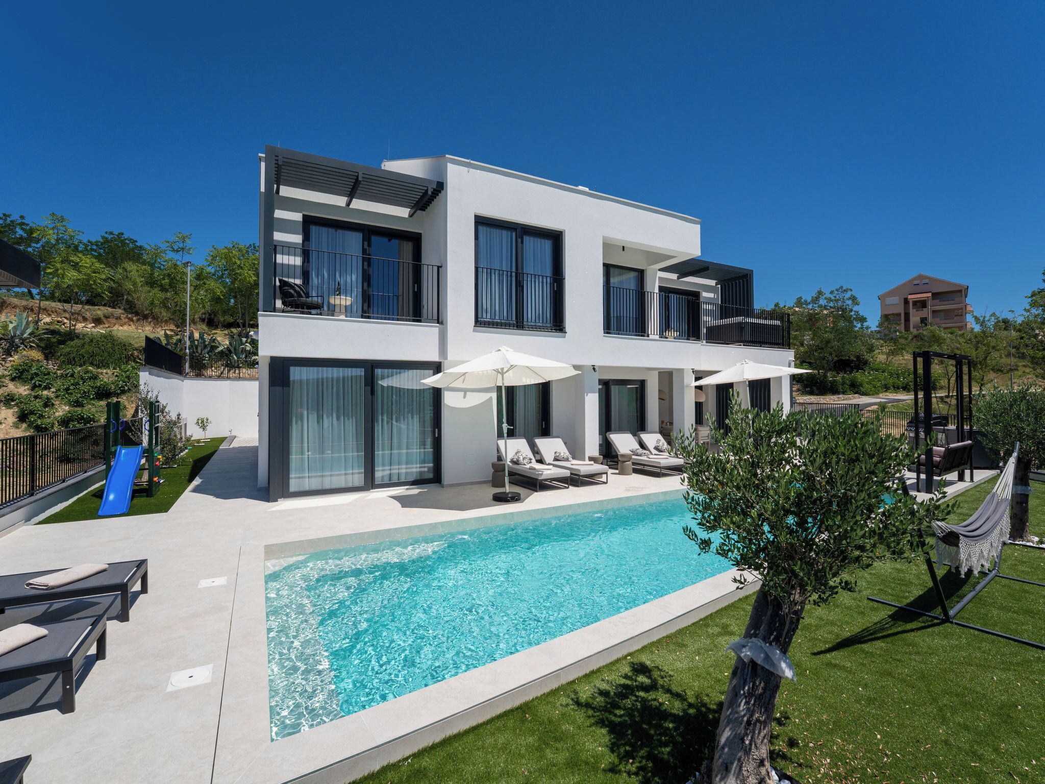 Ein modernes, zweistöckiges Haus mit Pool, Sitzgelegenheit im Freien und einem Garten.