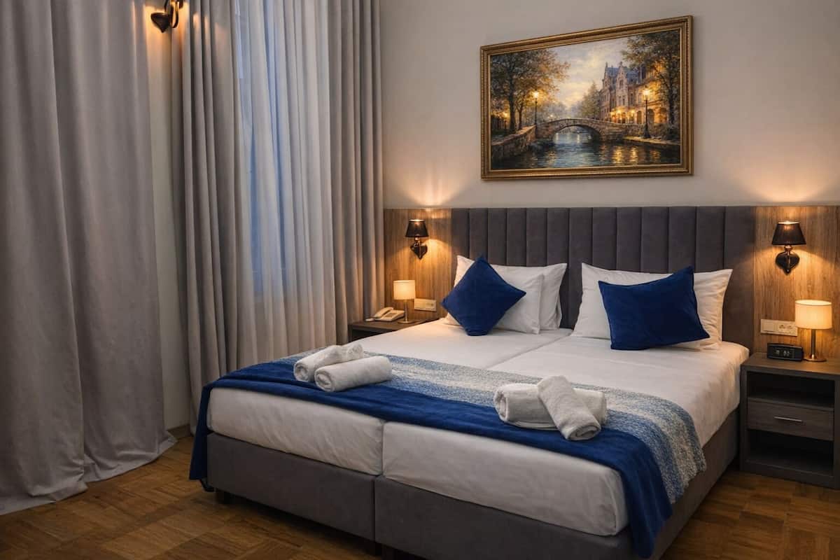 Habitación de hotel con una cama grande, dos mesitas de noche con lámparas, un cuadro en la pared y vistas a un puente.