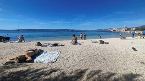 Une plage où l’on peut voir des gens se prélasser au soleil et nager, une eau d’un bleu limpide et des bateaux au loin.