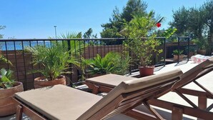 Une terrasse dotée de chaises longues et de plantes en pot, donnant sur une étendue d’eau.
