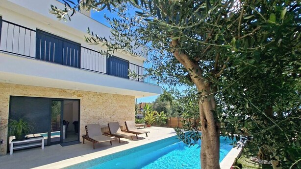 Une maison moderne dotée d’une piscine, d’un espace salon extérieur et d’un arbre.