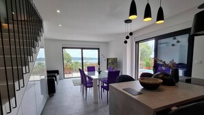 Une cuisine moderne avec un coin repas, de grandes fenêtres et une vue sur l’extérieur.