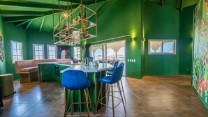 A modern kitchen with a bar area, green walls, and a view through large windows. - The Ambassador Full Building (Jan Thiel)