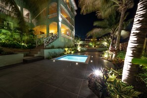 A pool area with a staircase leading to a balcony, surrounded by palm trees and plants. - The Ambassador Full Building (Jan Thiel)