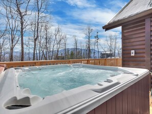 Ein Whirlpool auf einer Holzterrasse mit Blick auf Berge und Bäume.