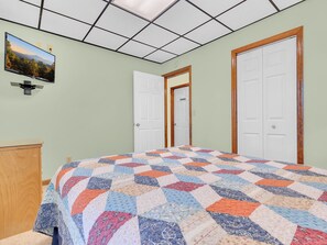 A bedroom with a large bed, two white doors, a wooden dresser, and a ceiling with a grid pattern. - Mountain Views- Game Room -Hot Tub - Pet-Friendly (Gatlinburg)