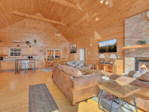 Un intérieur de cabine spacieux, avec un plafond en bois, une cheminée en pierre, un coin repas et un salon confortable doté d’un canapé et d’une table basse.
