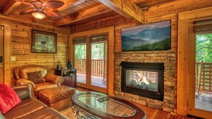 A cozy cabin interior with a stone fireplace, leather furniture, and a scenic mountain view. - Downtown Cabin|Private Pool|Hot Tub|Game Room (Pigeon Forge)