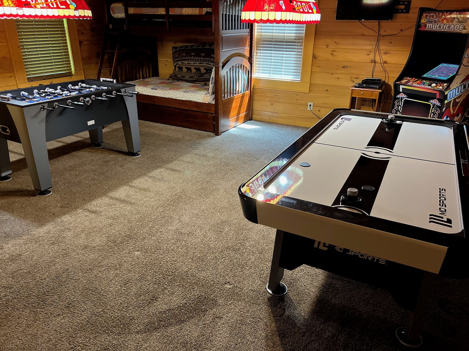 A room with a foosball table, a pool table, and a gaming console.