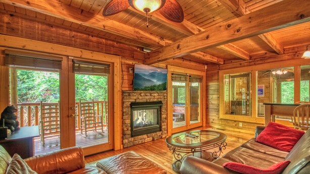 A wooden cabin interior with a fireplace, leather furniture, and large windows. - Downtown Cabin|Private Pool|Hot Tub|Game Room (Pigeon Forge)