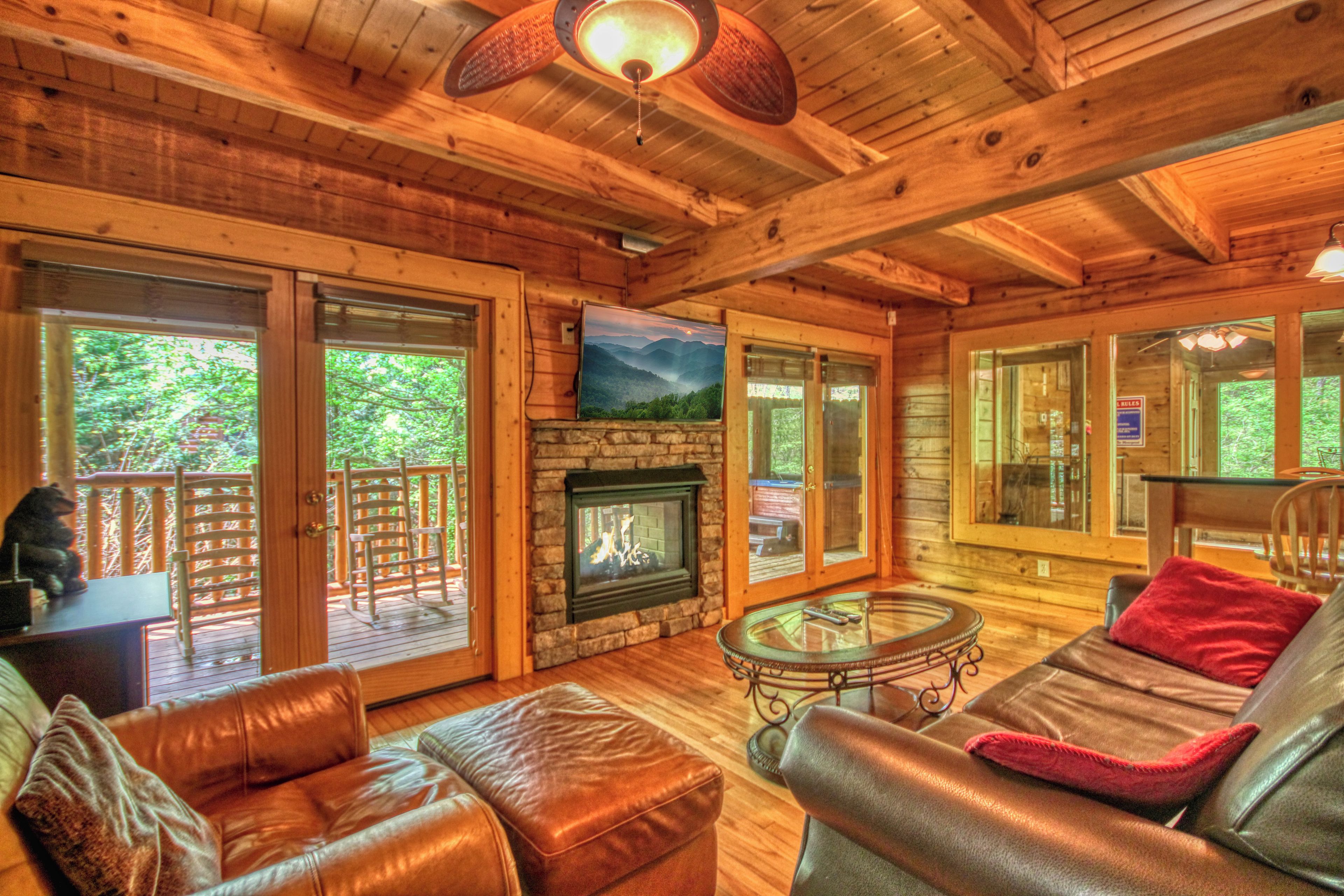 A wooden cabin interior with a fireplace, leather furniture, and large windows.
