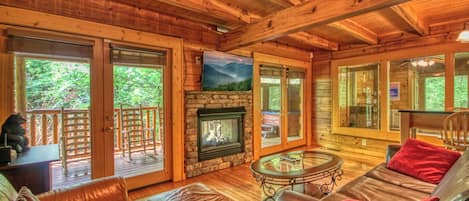 A wooden cabin interior with a fireplace, leather furniture, and large windows.