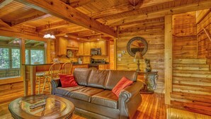 A cozy cabin interior with a leather sofa, wooden dining table, and a kitchen area. - Downtown Cabin|Private Pool|Hot Tub|Game Room (Pigeon Forge)