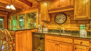 A wooden cabin kitchen with a clock, wooden cabinets, a dishwasher, and a coffee maker. - Downtown Cabin|Private Pool|Hot Tub|Game Room (Pigeon Forge)