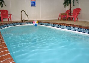 Ein Hallenbad mit gefliestem Rand, einem Hinweisschild zu den Poolregeln und roten Stühlen rund um den Poolbereich.
